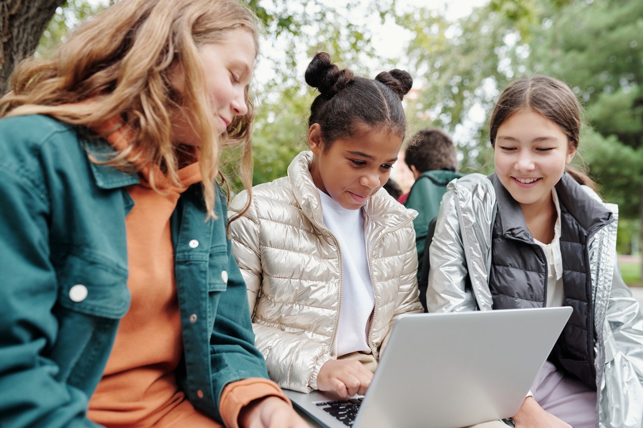 Dzieci z laptopem siedzą w parku i uczą się kodowania